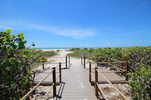 Une promenade en bois menant à une plage, avec un ciel dégagé.
