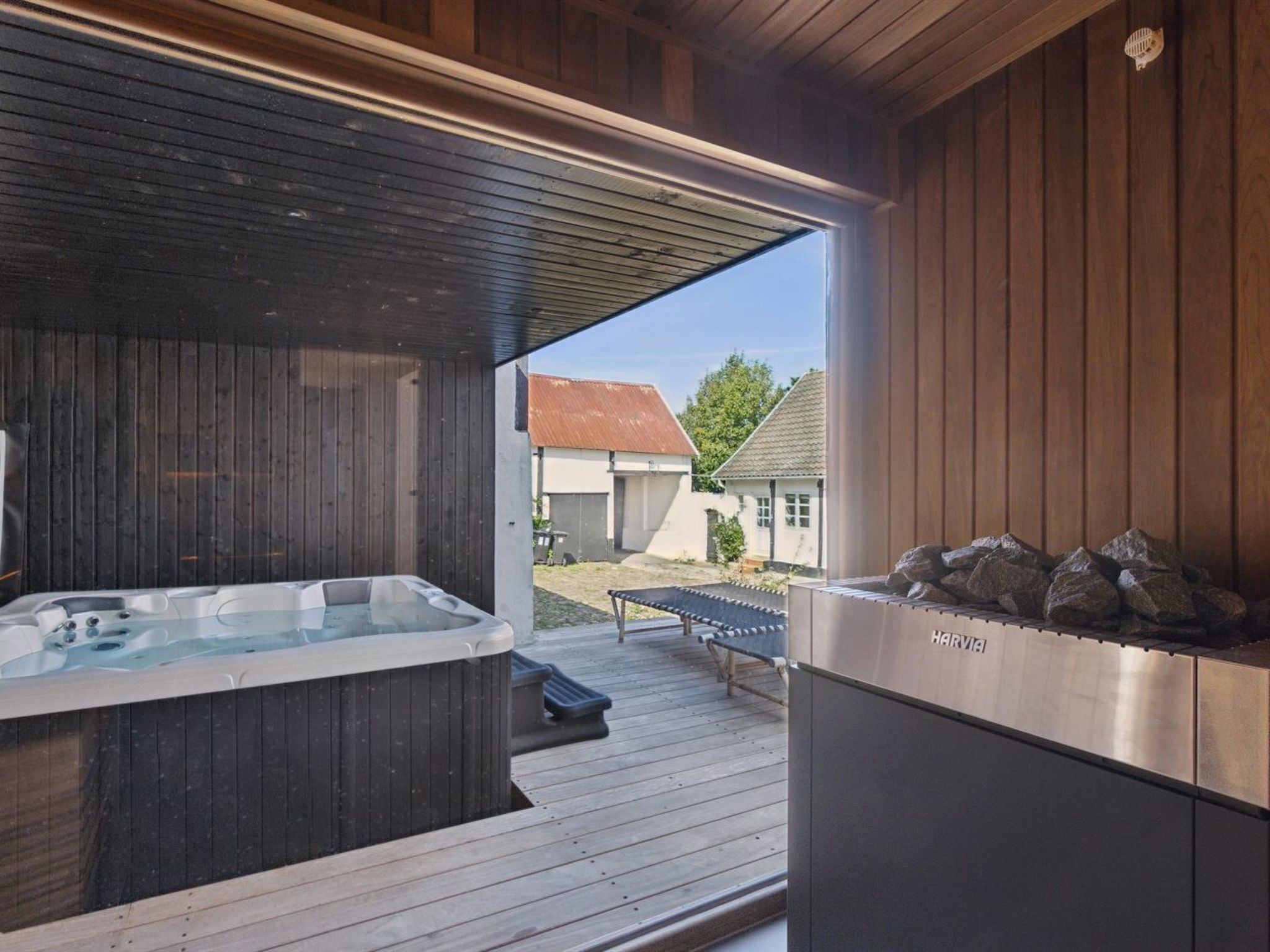 A hot tub and a sauna in a wooden outdoor area with a view of houses in the background.