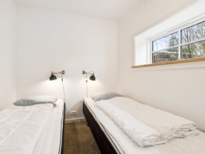 Een kleine, schone kamer met twee eenpersoonsbedden, een raam met uitzicht op bomen en twee wandlampen.
