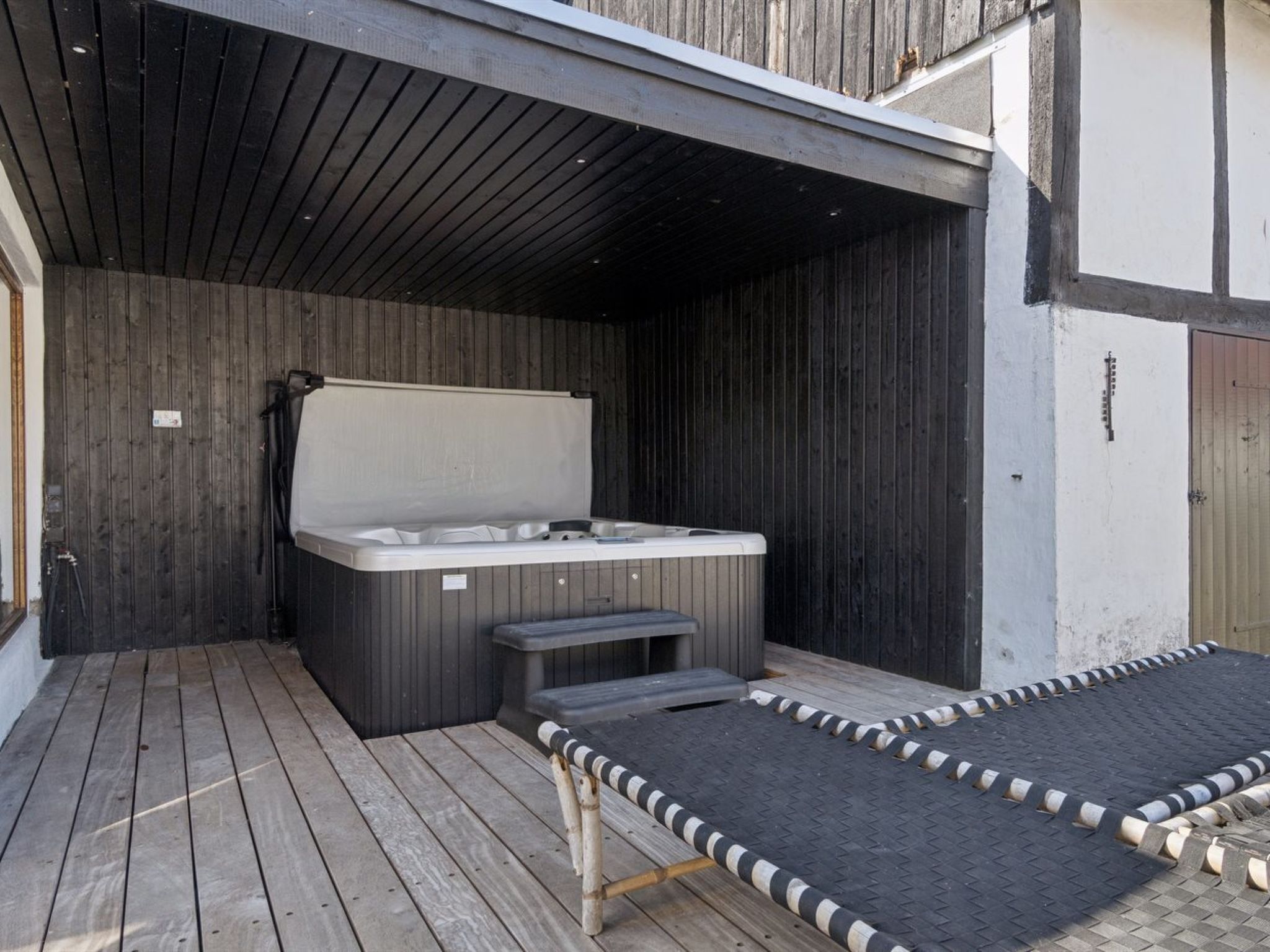 A hot tub under a wooden pergola with a wooden deck and a metal ramp leading to it.
