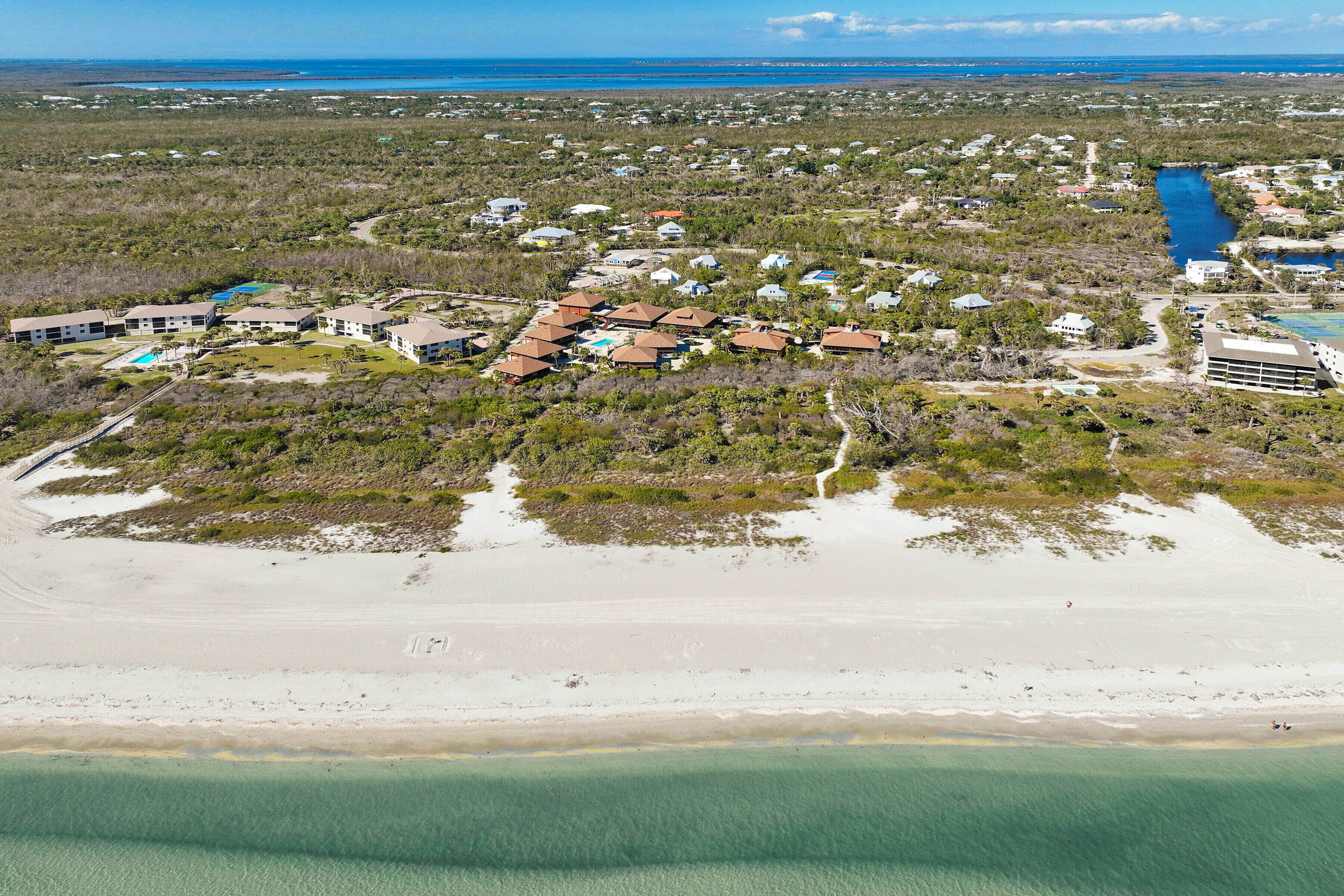 Vue aérienne d’une zone résidentielle côtière, avec des maisons, une plage et une vue dégagée sur l’océan.