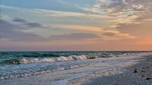 Una playa con olas, cielo despejado y un atardecer.