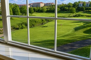 Blick auf einen Golfplatz mit Fahnenstange, umgeben von Grünflächen und Gebäuden im Hintergrund.