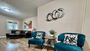 Una sala de estar con un sofá modular, dos sillones turquesa, una mesa de centro redonda y una obra de arte en la pared.