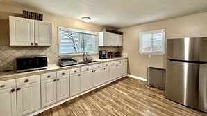 Una cocina con armarios blancos, un refrigerador de acero inoxidable, un microondas y un lavamanos.