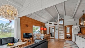 A spacious living area with a large sofa, a dining table, and a kitchen area with white cabinets and wooden accents. - "Oddger" - 250m to the fjord by Interhome (Skjern)