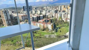A balcony with a view of a cityscape, two white stools, and a metal railing. - 18th Floor Luxury Condo With Pool (Skopje)
