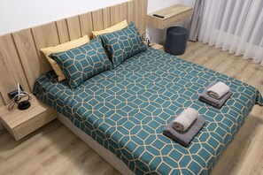Una cama bien tendida con una colcha de estampado geométrico, una mesita de noche con lámpara y un teléfono en la pared.