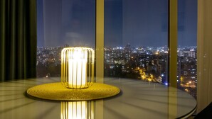 A table with a lamp in a room with a city view through large windows. - 18th Floor Luxury Condo With Pool (Skopje)