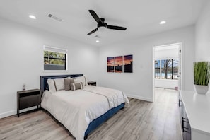 Un dormitorio moderno con cama, ventilador de techo, ventana y un cuadro.