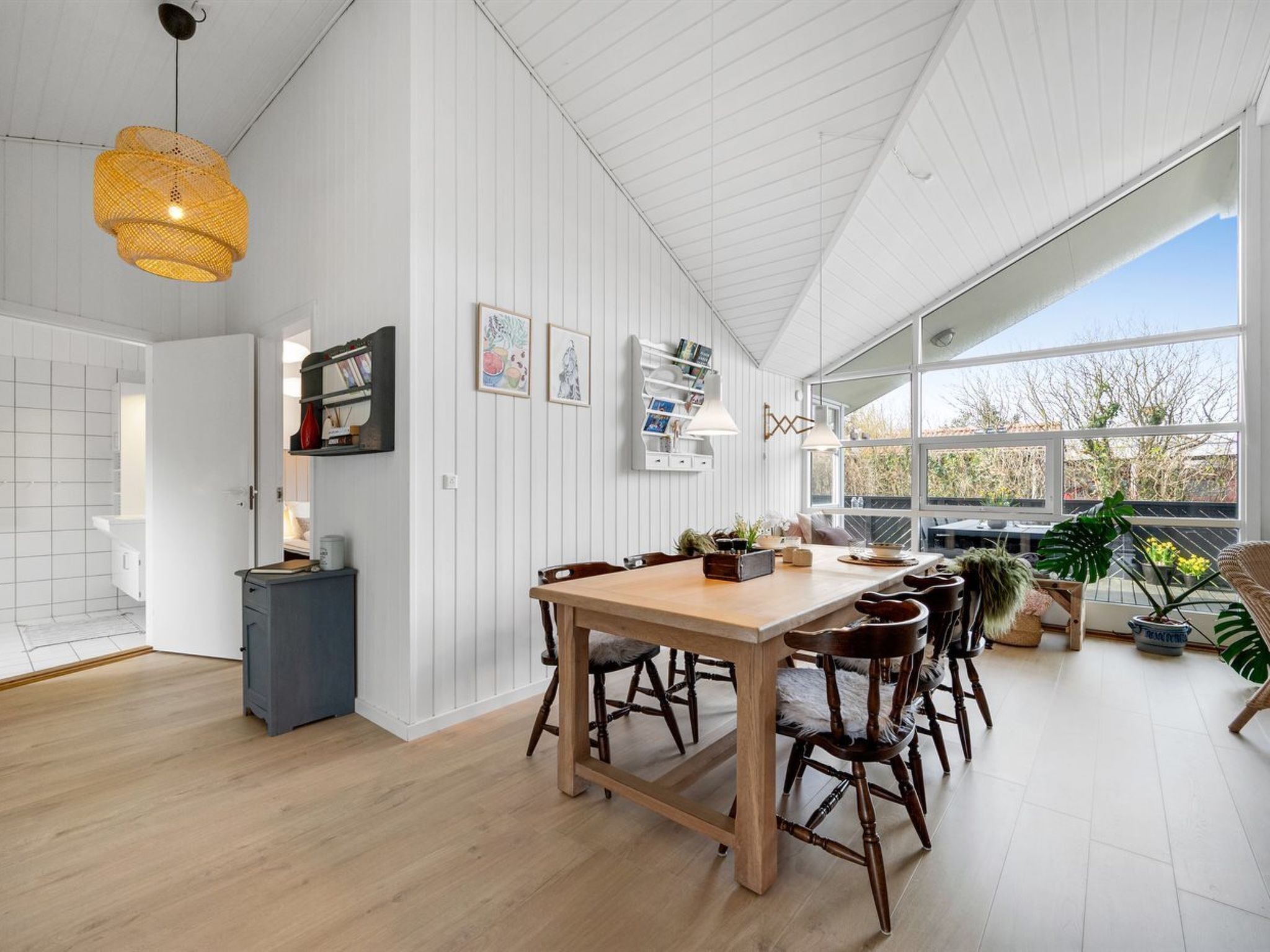 A modern kitchen with white walls, wooden flooring, and a large window.