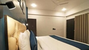 A hotel room with a bed, a headboard, a bedside table, and a window with curtains. - Noida Metro Hotel By Wamson (Noida)