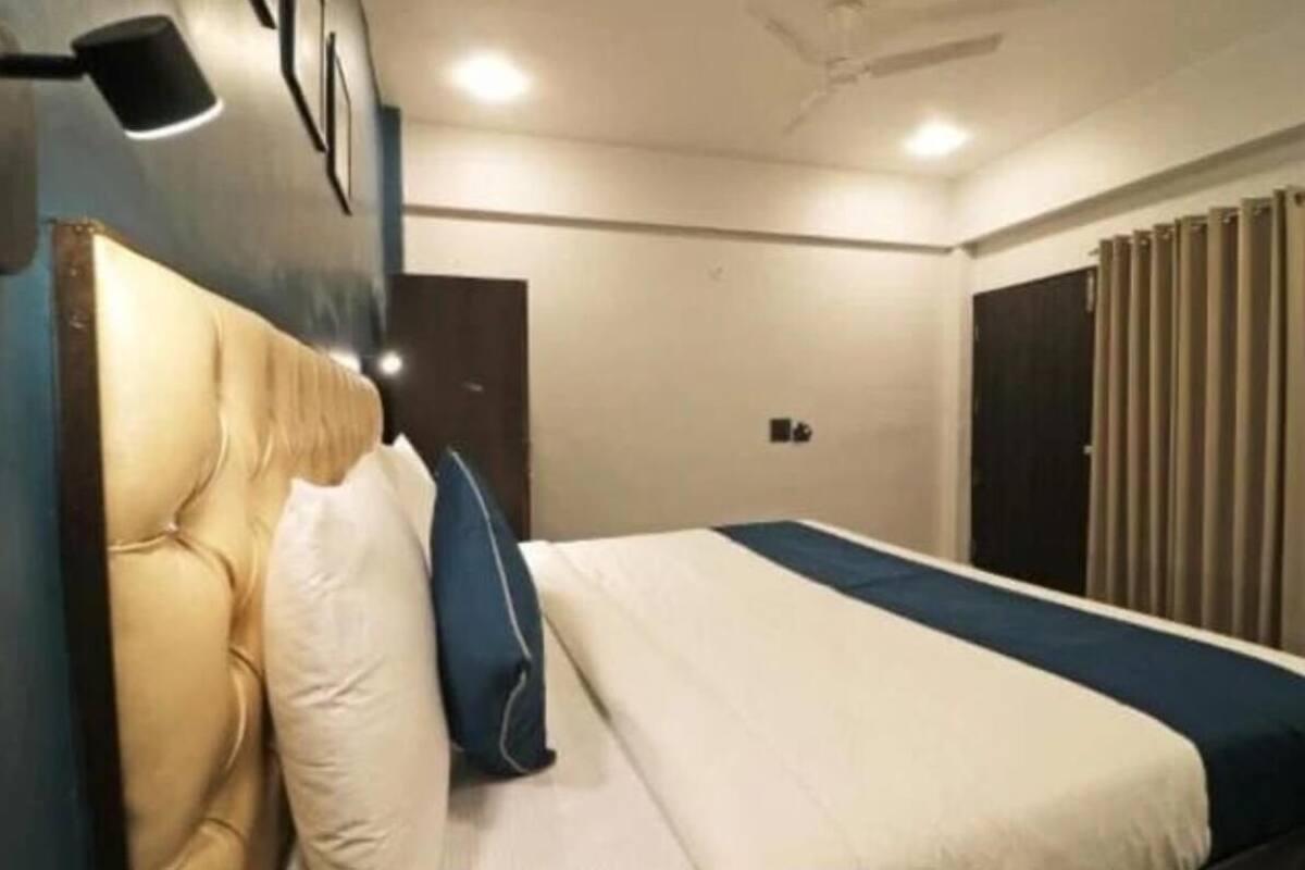 Habitación de hotel con cama, cabecero, mesita de noche y ventana con cortinas.