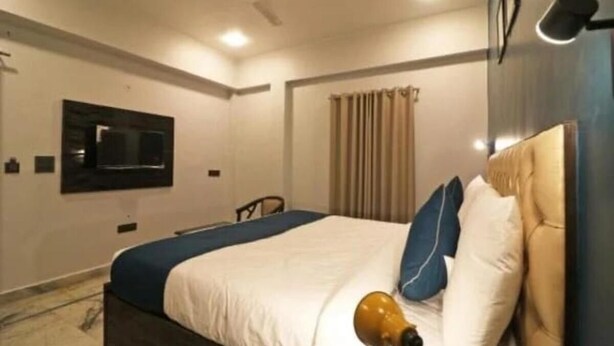 Habitación de hotel con cama, escritorio, silla, televisor y ventana con cortinas.