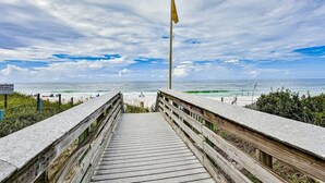 Une promenade en bois mène à une plage où se trouvent un mât et un panneau indiquant qu’il est interdit de s’approcher des dunes.