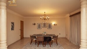 A dining area with a marble floor, a chandelier, framed artwork, and a large window with curtains. - villa in deplomaseen district (Sheikh Zayed City)