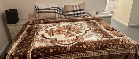 A neatly made bed with a patterned bedspread, two pillows, a bedside table with a lamp, and a bathroom visible in the background.