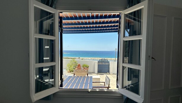 An open window with a view of the ocean and a patio area with a table and chairs.