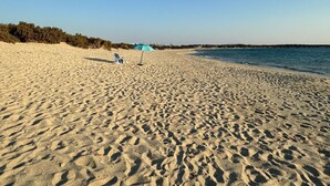 A sandy beach with footprints, a single beach chair, and a blue umbrella.