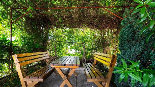 A wooden bench and table set under a pergola with a view of a garden. - Apartment in Rogoznica near Miline Beach (Rogoznica)