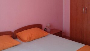 A single bed with two orange pillows, a bedside table with a lamp, and a wardrobe with two doors. - Apartment in Rogoznica near Miline Beach (Rogoznica)