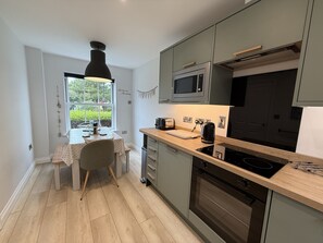 Uma cozinha compacta com mesa de jantar, micro-ondas, forno e janela com vista para vegetação.