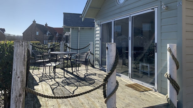 Een houten terras met een tafel, stoelen, een touwbescherming en een schuifdeur van glas.