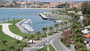 Uma marina com barcos atracados, uma estrada sinuosa e uma cidade costeira ao fundo.