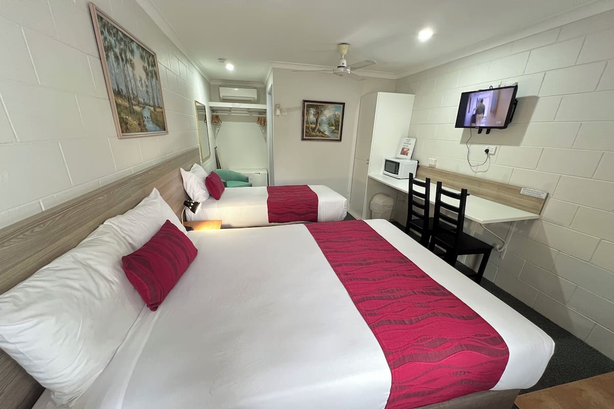 Une chambre d’hôtel avec deux lits, un bureau, une chaise, une télévision et un ventilateur de plafond.