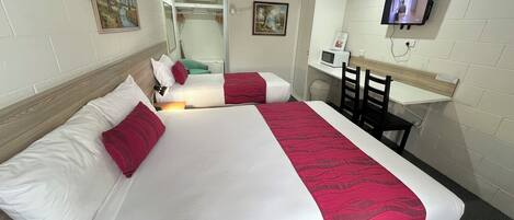 A hotel room with two beds, a desk, a chair, a television, and a ceiling fan.