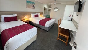Een hotelkamer met twee bedden, een bureau, een stoel, een televisie en een plafondventilator.