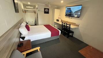 A compact hotel room with a bed, a desk, a TV, and a small seating area.