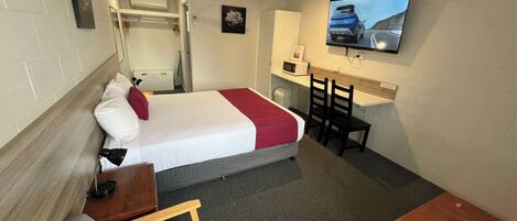 A compact hotel room with a bed, a desk, a TV, and a small seating area.