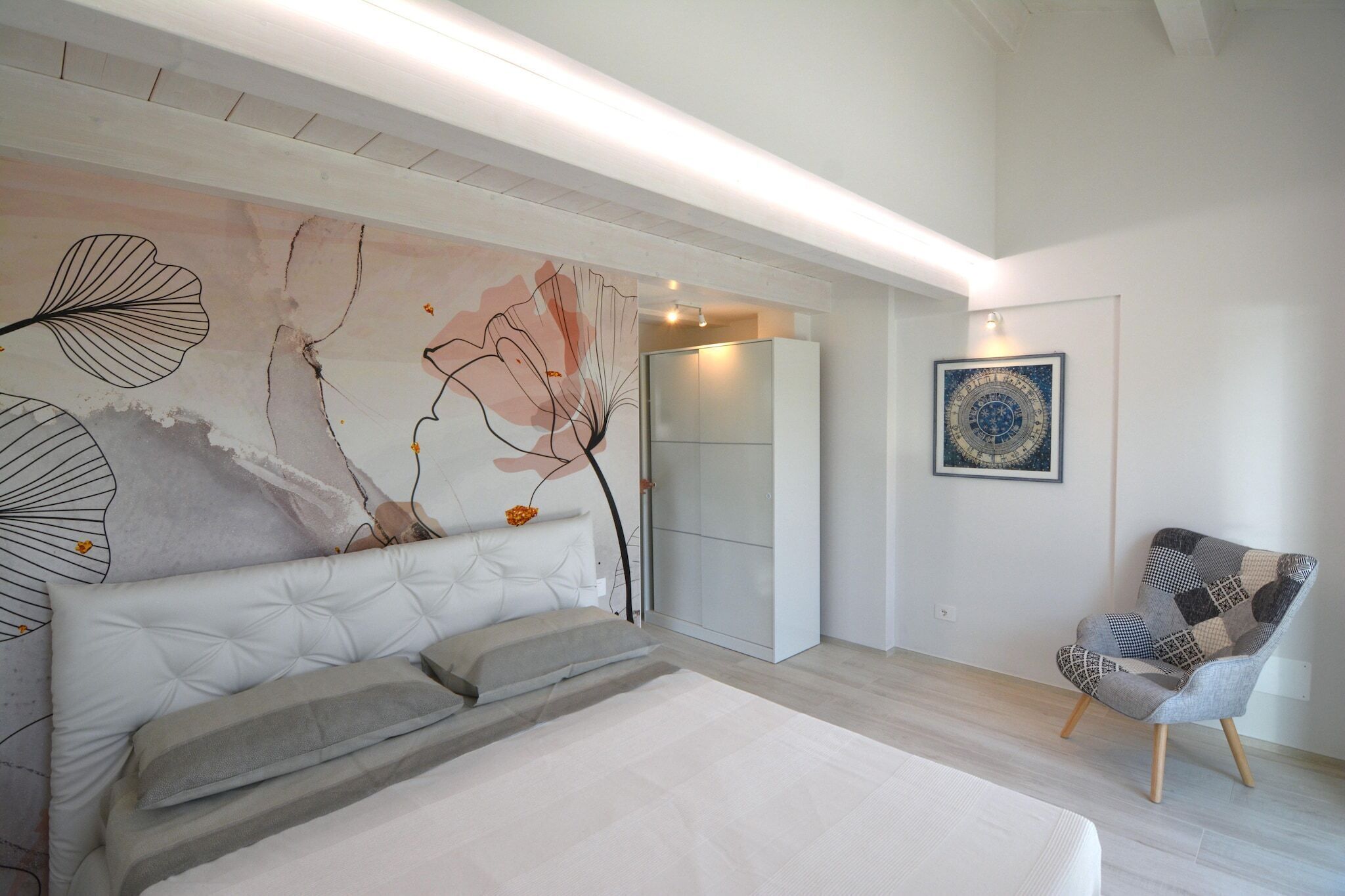 Une chambre moderne avec un grand lit, un canapé, un fauteuil et un mur orné d’œuvres d’art abstraites.