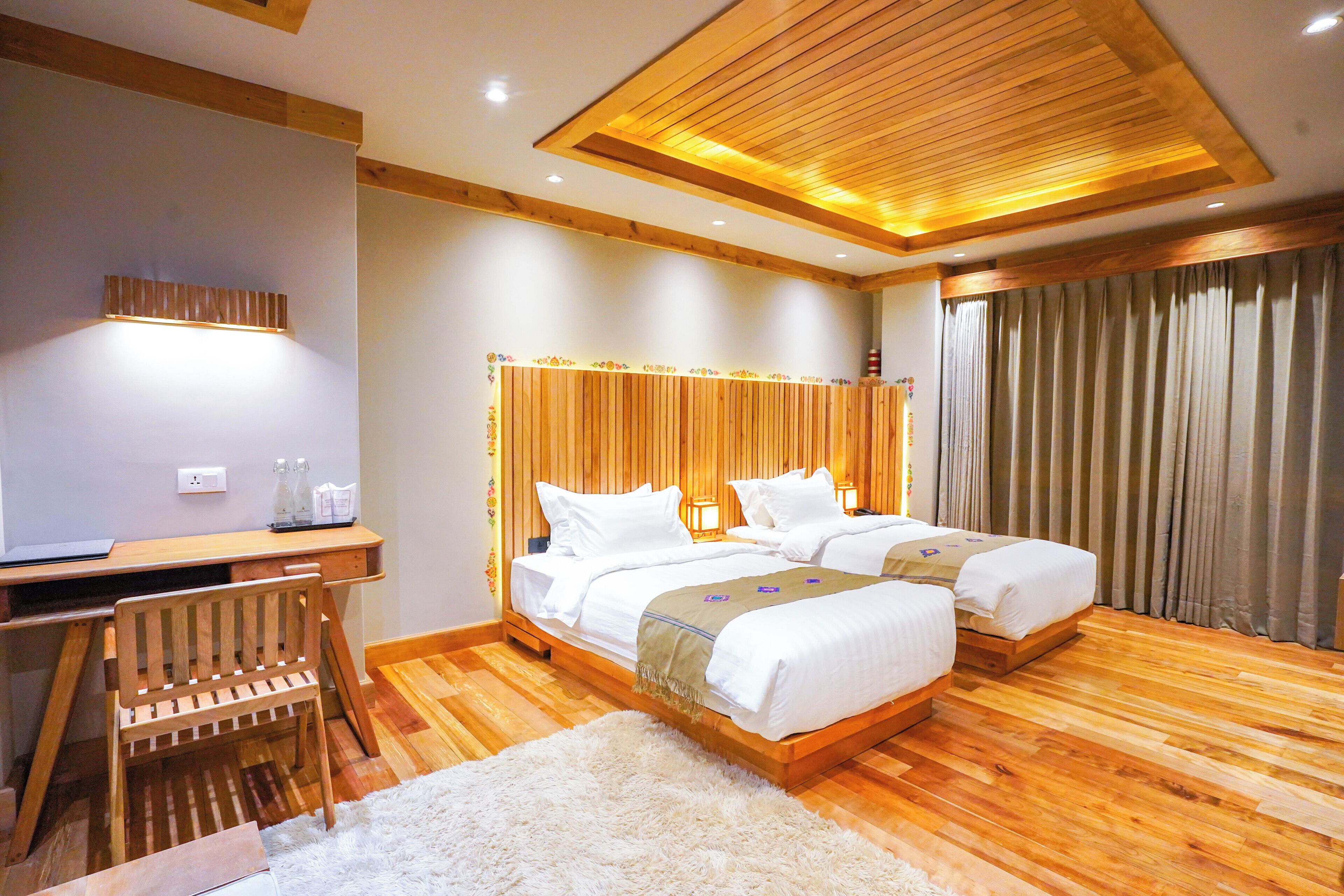 A hotel room with a wooden floor, two beds, a desk, and a chair.