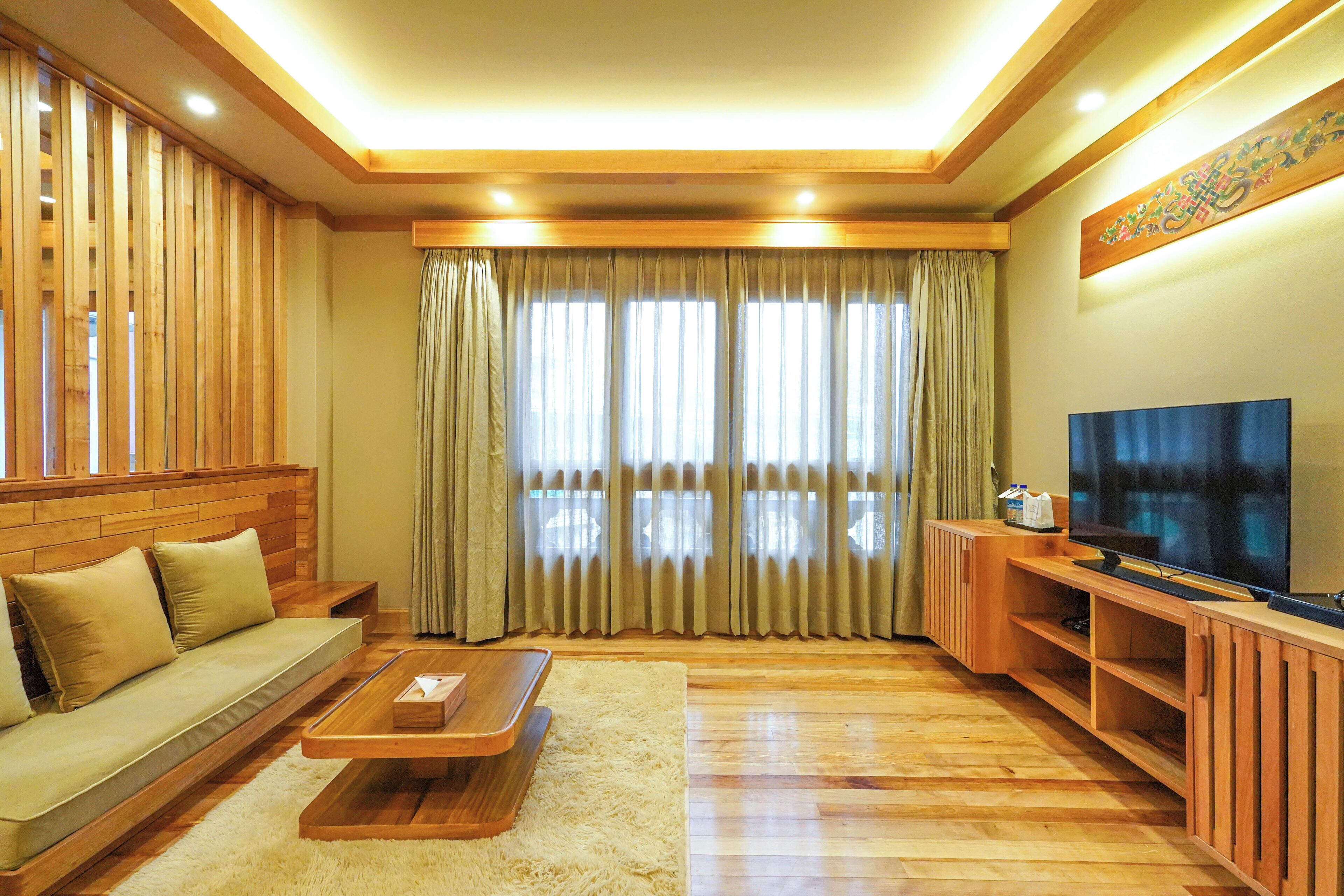 A living room with a sofa, coffee table, TV, wooden decor, and large windows with curtains.