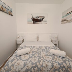 Une chambre à coucher avec un lit, deux tables de chevet, un tableau représentant un bateau et une couvre-lit à motifs floraux.