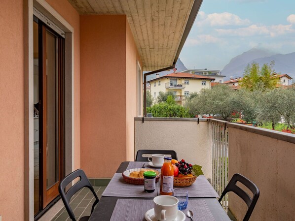 A balcony with a table set for breakfast, including bread, fruit, and beverages.