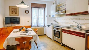 A compact kitchen with a dining table, oven, sink, and a TV mounted on the wall. - Nice apartment for 4 guests with WIFI and TV (Pergine Valsugana)