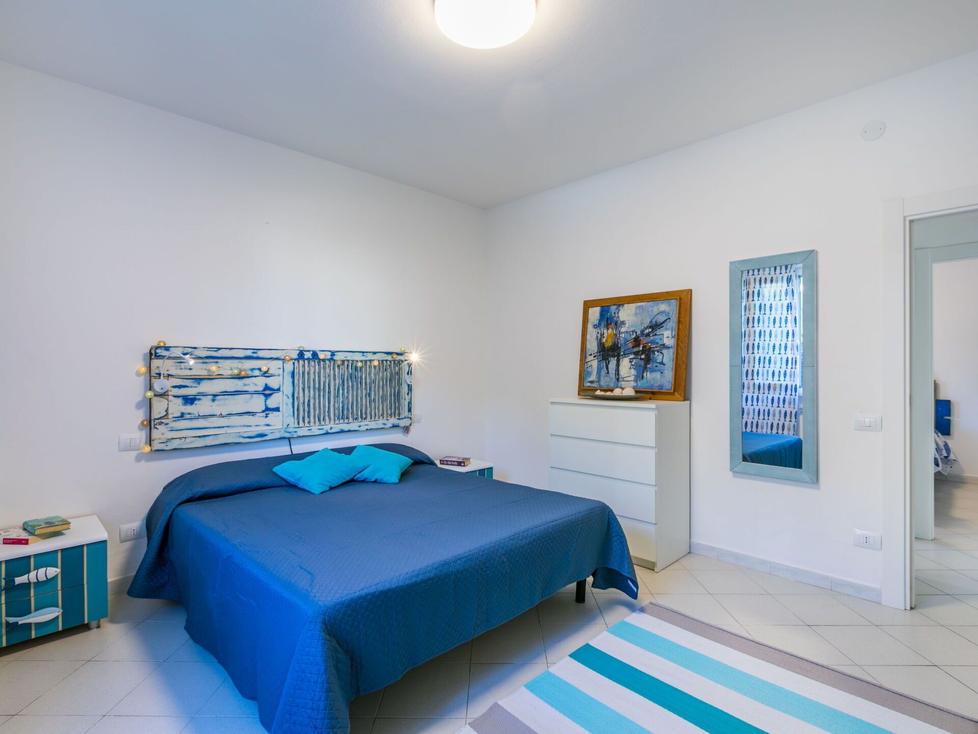 A bedroom with a bed, a dresser, a mirror, and artwork on the walls.