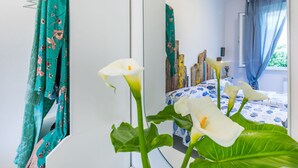 A modern bedroom with a large mirror, floral curtains, and a bed with a blue and white patterned bedspread. - Lovely apartment for 4 people with WIFI, A/C, TV, balcony and pets allowed (Cecina)