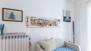A room with a white radiator, a chair with a patterned cushion, a wall-mounted light fixture, and a framed picture of a sailboat. - Lovely apartment for 4 people with WIFI, A/C, TV, balcony and pets allowed (Cecina)