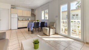 A modern kitchen with a dining area, a sliding glass door to a balcony, and a green plant on a table. - Lovely apartment for 3 people with A/C, WIFI, pool, TV and terrace (Empuriabrava)