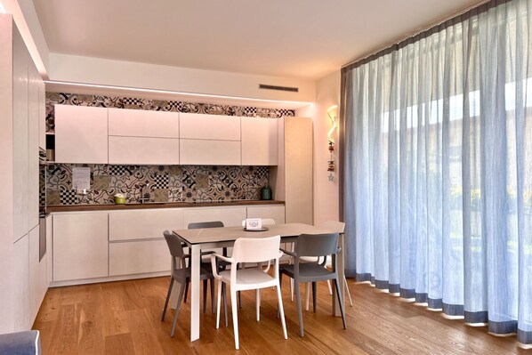A modern kitchen with white cabinets, a patterned backsplash, and a dining area with a table and chairs. - Large, bright and modern flat with an incredible view on lake Garda in Malcesine (Malcesine)