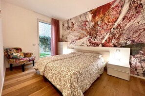 A bedroom with a large bed, a chair, a dresser, and a wall with a floral tapestry. - Large, bright and modern flat with an incredible view on lake Garda in Malcesine (Malcesine)
