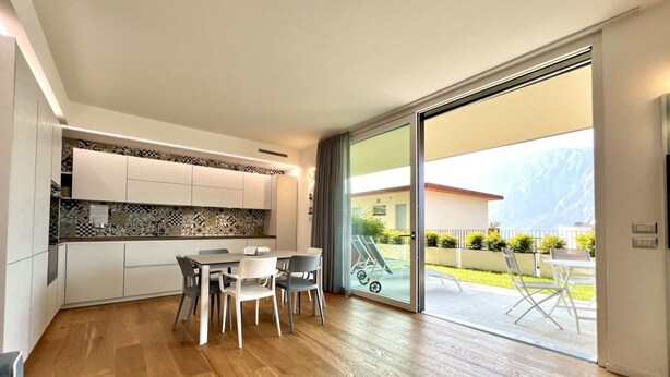 A modern kitchen with white cabinets and a patterned backsplash, a dining area with a table and chairs, and a sliding glass door leading to an outdoor patio with a view of a mountain. - Large, bright and modern flat with an incredible view on lake Garda in Malcesine (Malcesine)