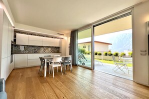 A modern kitchen with white cabinets and a patterned backsplash, a dining area with a table and chairs, and a sliding glass door leading to an outdoor patio with a view of a mountain. - Large, bright and modern flat with an incredible view on lake Garda in Malcesine (Malcesine)