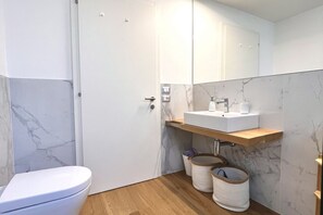 A modern bathroom with a white toilet, a wooden floor, a marble backsplash, a white sink with a wooden shelf above, and a mirror above the sink. - Large, bright and modern flat with an incredible view on lake Garda in Malcesine (Malcesine)