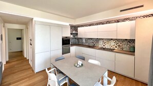 A modern kitchen with white cabinets, a grey countertop, and patterned backsplash. There is a dining table with chairs and a small island with a sink. - Large, bright and modern flat with an incredible view on lake Garda in Malcesine (Malcesine)