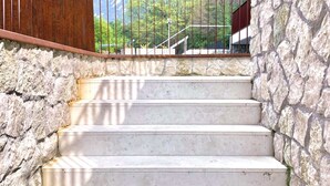 A set of stone steps leading up to a wooden door, with a metal railing and a view of greenery in the background. - Large, bright and modern flat with an incredible view on lake Garda in Malcesine (Malcesine)